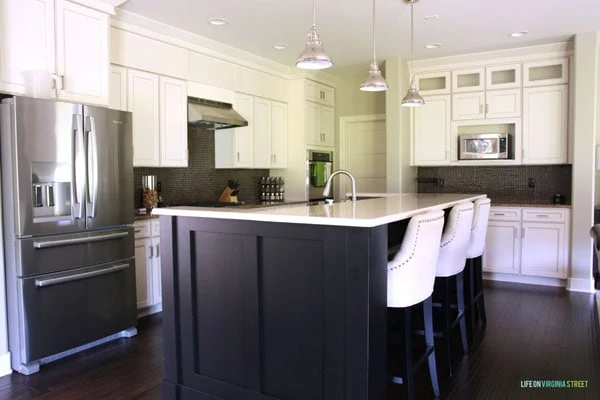 A large stainless steel fridge, a dark kitchen island with a white countertop and white cupboards.