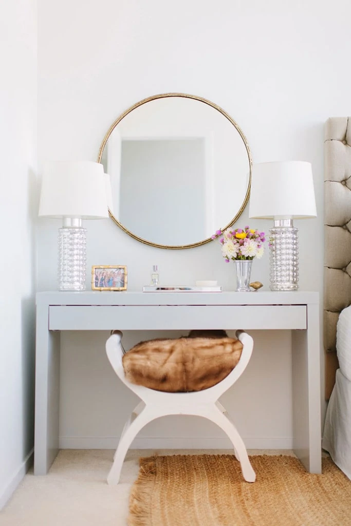 Beautiful round mirror above a vanity flanked with two crystal lamps with white shades. 