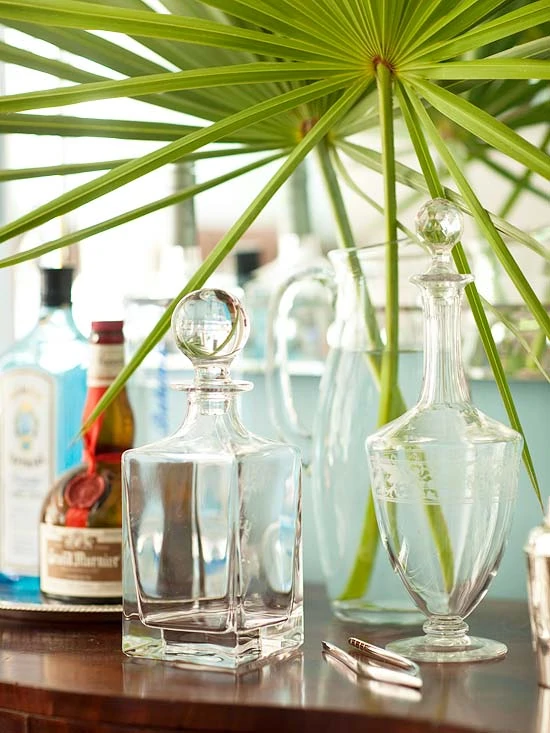 Decanters on top of a wood bar with palm fronds over top of it.
