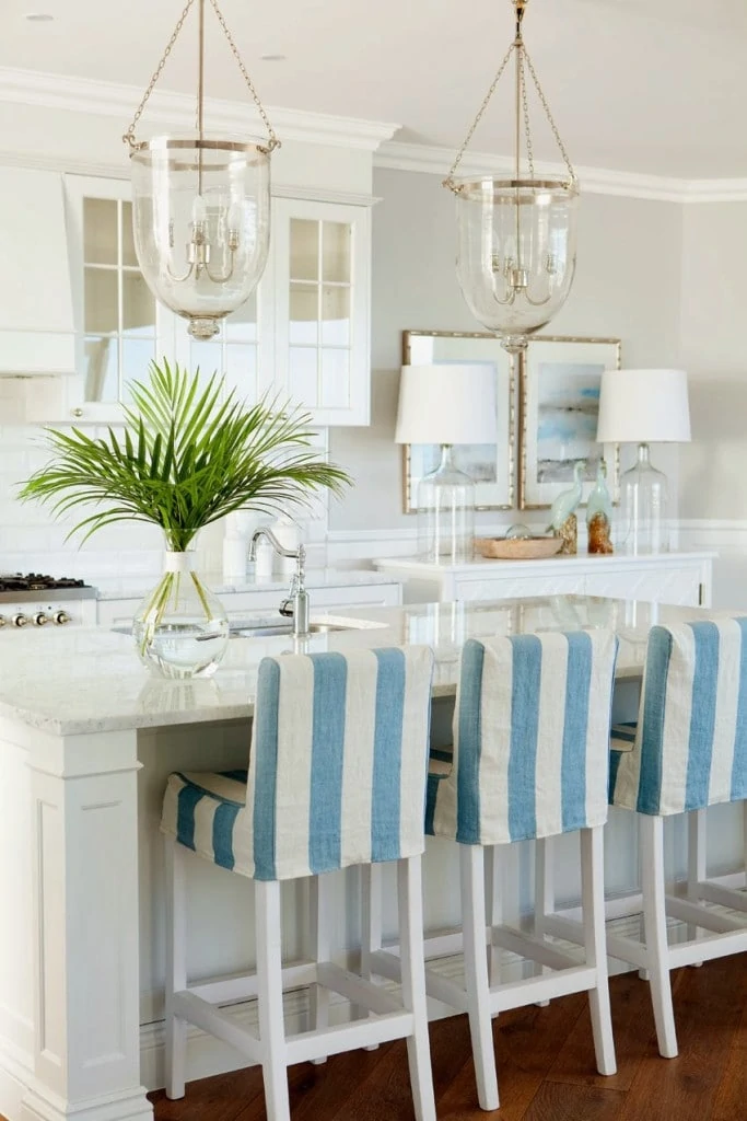 White kitchen with blue and white striped chairs and palm fronds on the island.