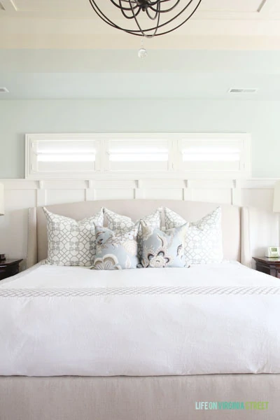 A master bedroom painted Sherwin Williams Sea Salt with a linen headboard and white bedding.
