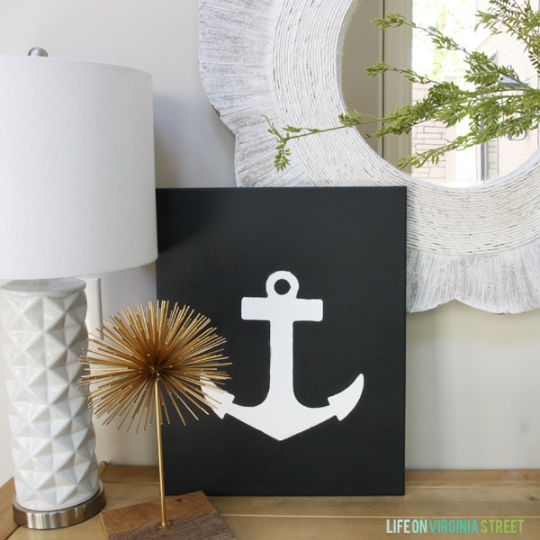 Anchor canvas art on the side table in the hallway with a white lamp beside it.