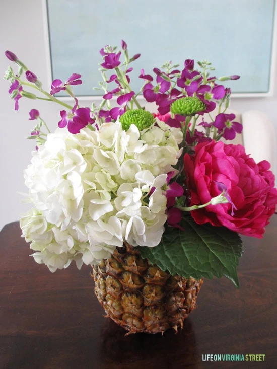 The flowers inside the pineapple vase on the table.