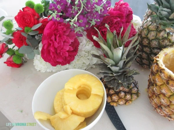 The cored pineapple, fresh pineapple slices and flowers on the counter.