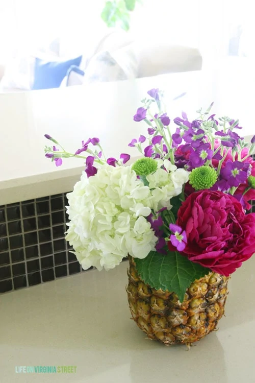 The fresh pineapple vase on the counter filled with flowers.