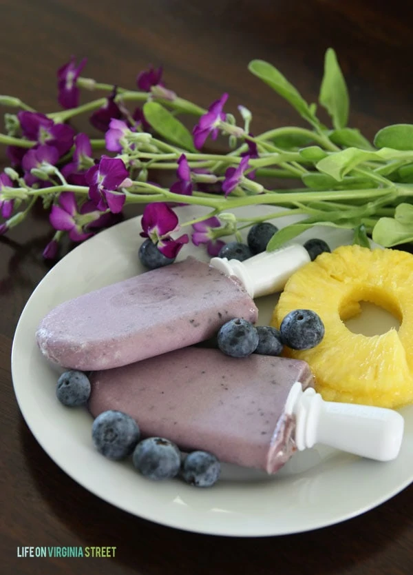  Blueberry Pineapple Coconut popsicles on a plate with flowers beside it.