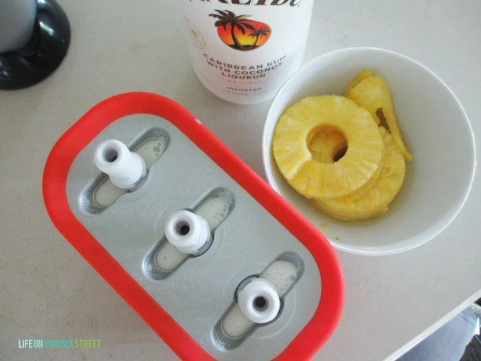 The popsicles in molds with the fresh pineapple in a bowl beside it.