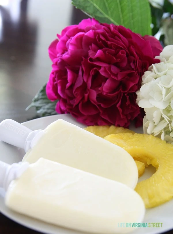  Pineapple Coconut popsicles with fresh flowers beside them.