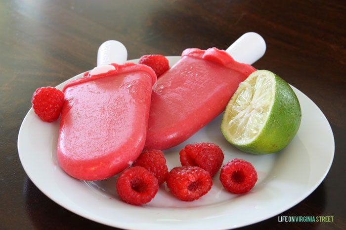 Raspberry Lime popsicles on a white plate with a lime and strawberries beside it.