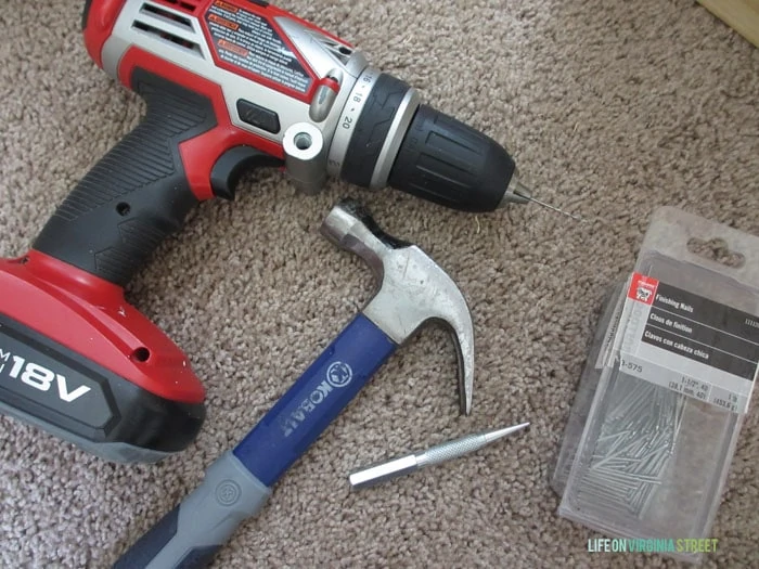 Red drill, blue hammer and drill bits on rug.