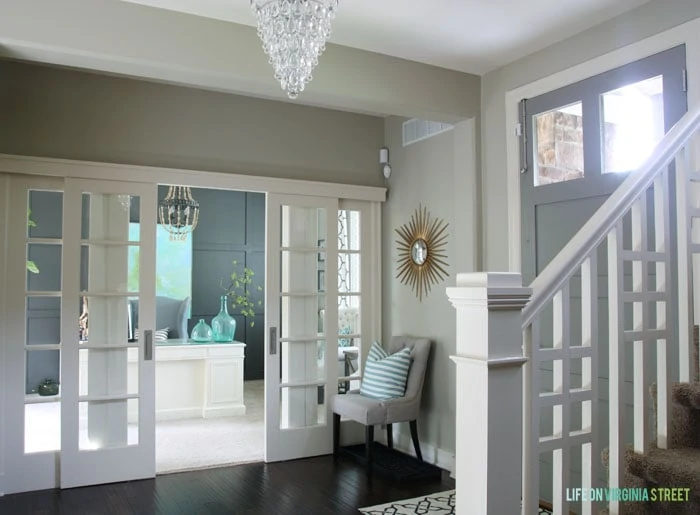 Sliding doors leading into office with a chandelier in foyer and soft muted whites and blues.