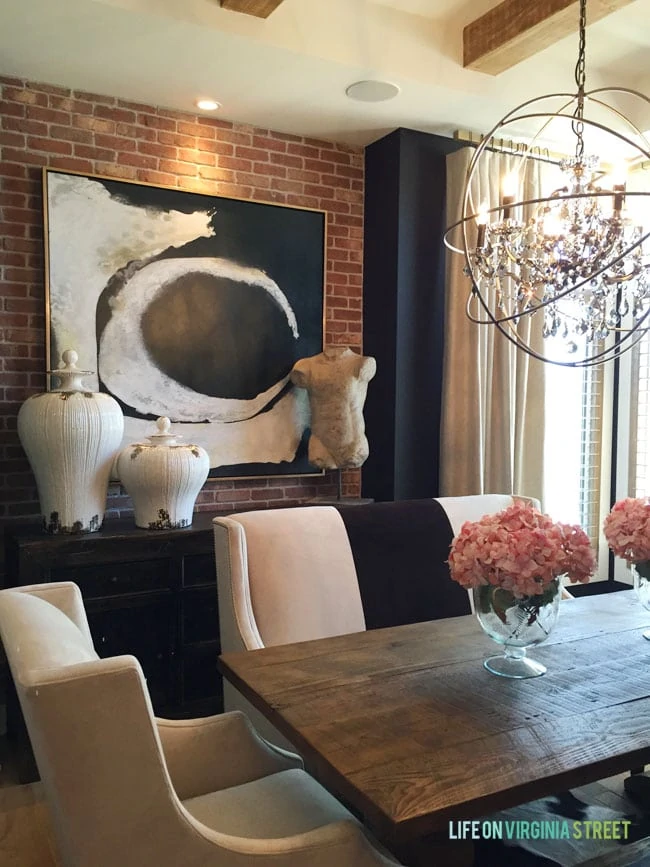 This gorgeous formal dining room features a red exposed brick wall, black walls, raw wood beams and a touch of glam with the orb chandelier.