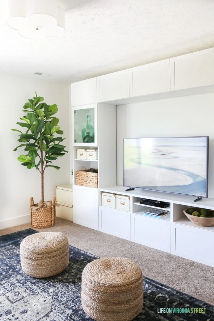 The tv room with neutral poufs and a white built in cabinet.