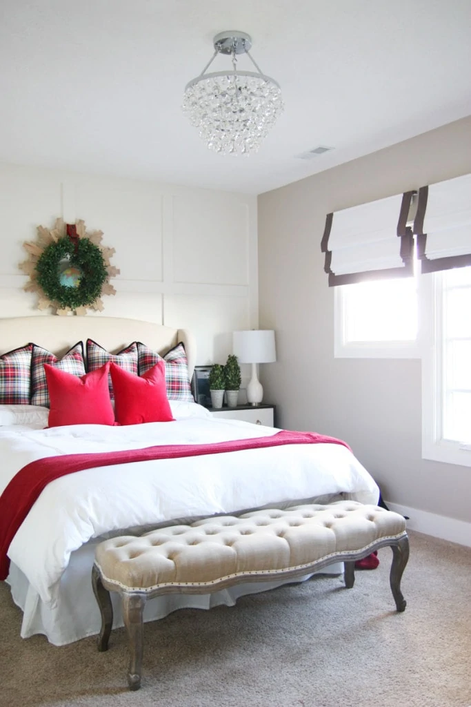 The white bedding with a red blanket on the bed, and red pillows.   A green wreath hangs above the bed.