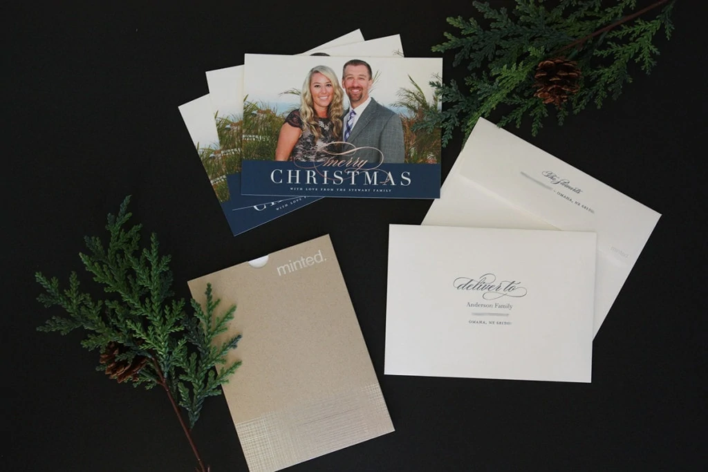 Christmas card on table with tree branches beside it.
