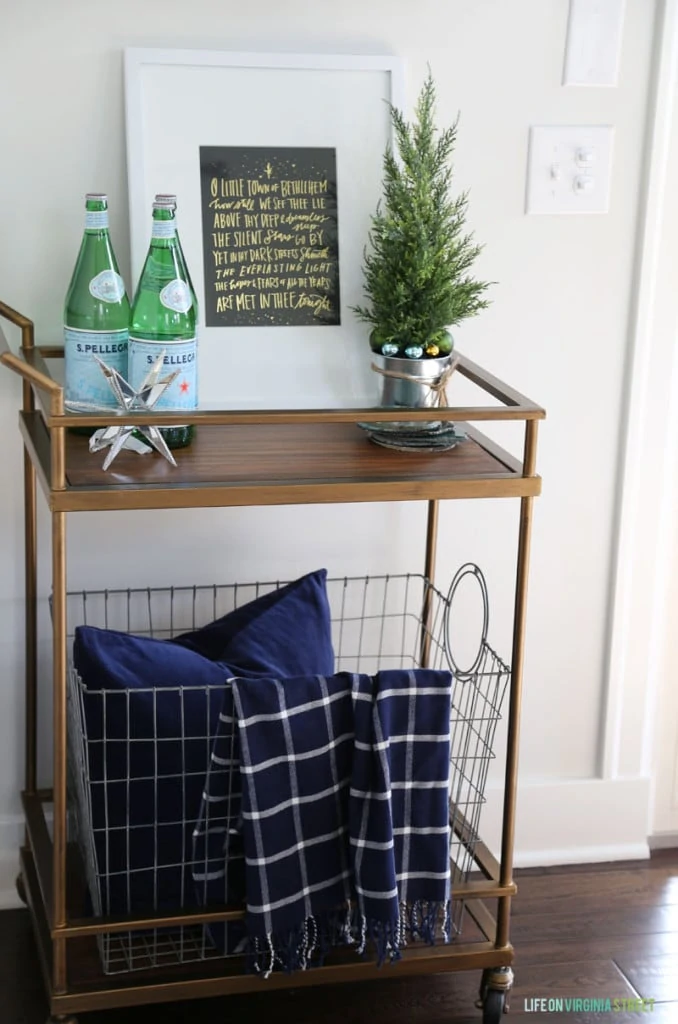 A brass and wood barcart decorated for Christmas with navy blue and green decor.