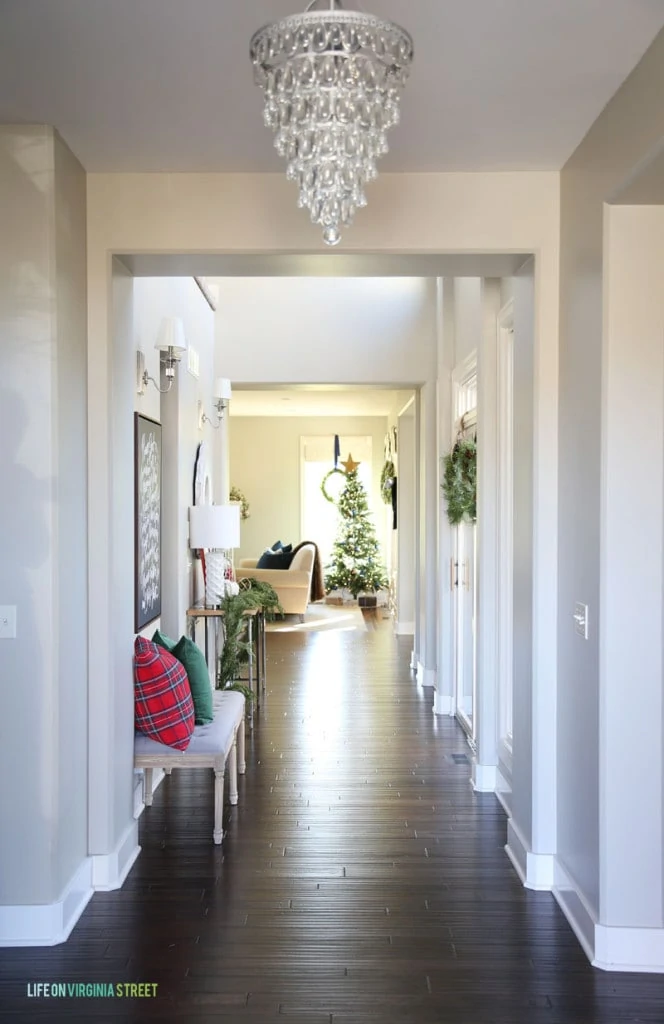 Christmas Entry Hallway with a crystal chandelier, dark hardwood floors, red plaid pillow and a view of a Christmas tree.