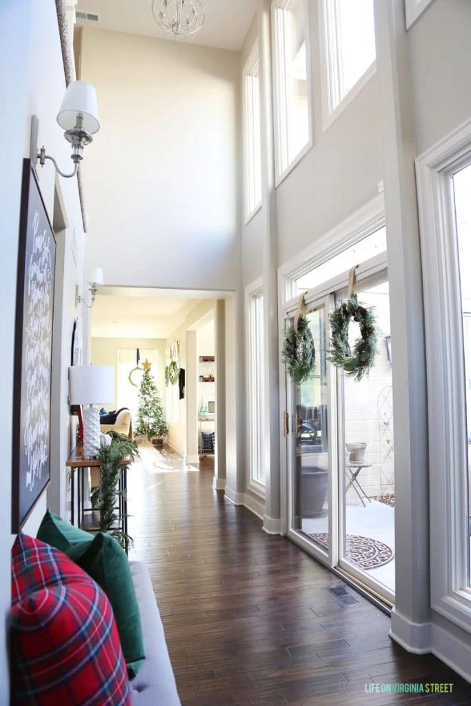 A Christmas hallway with wreaths hanging on the window and red plaid and green accents.