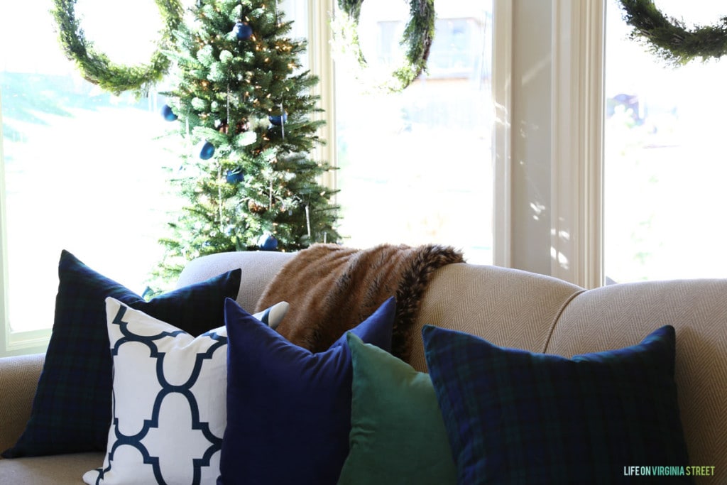 A combination of navy blue velvet, green velvet, and blue and white trellis pillows on a Christmas sofa.