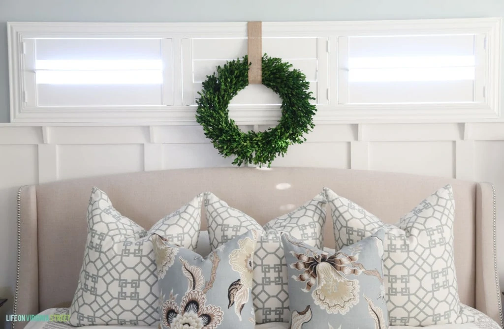 A beautiful blue and white Christmas bedroom with a boxwood wreath, trellis pillows and a linen headboard.