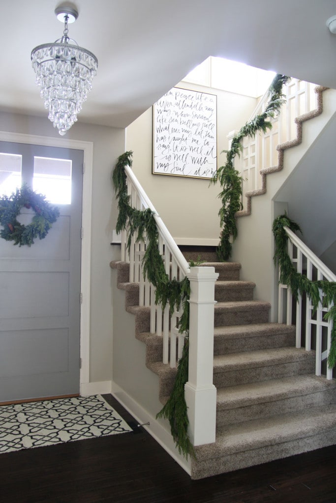 A Christmas staircase with fresh greenery and a gorgeous "It Is Well With My Soul" canvas on the wall.