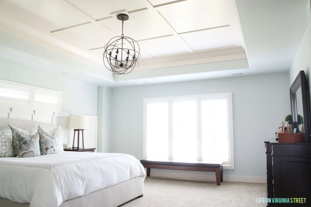 Light blue walls in bedroom with chandelier above white bed.