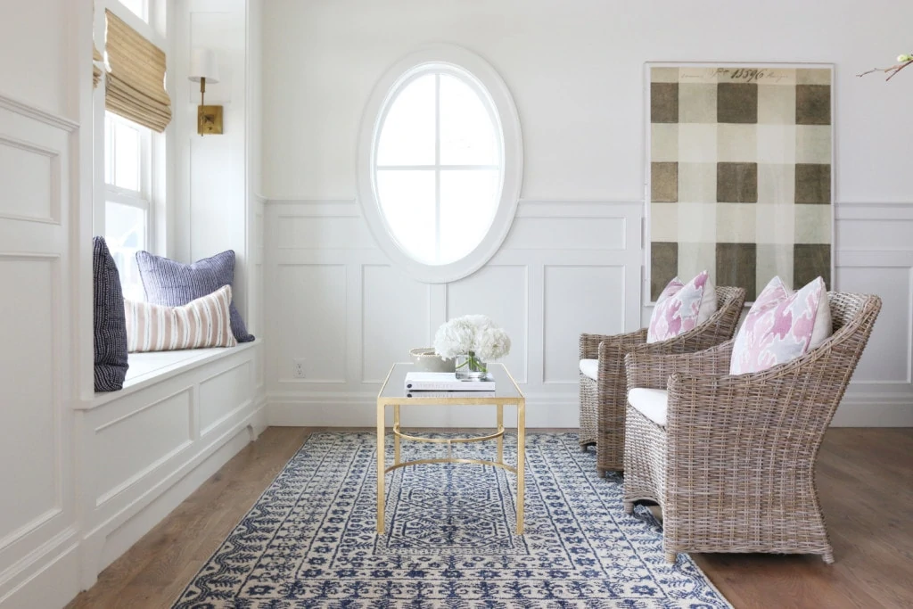 Studio room with oval window, a blue rug, wicker chairs and pillows on the window sill.