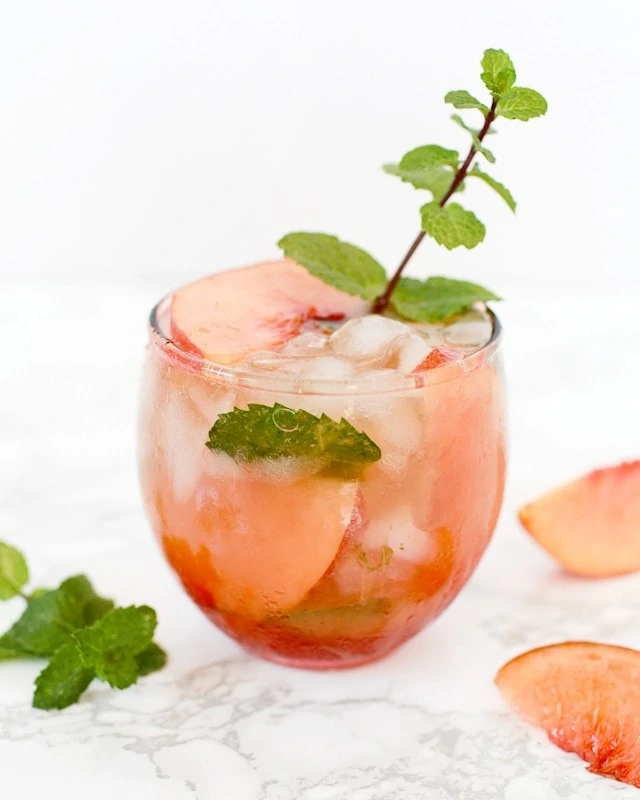 Basil-Mint Peach Bourbon Smash with a sprig of mint and peach in the glass.