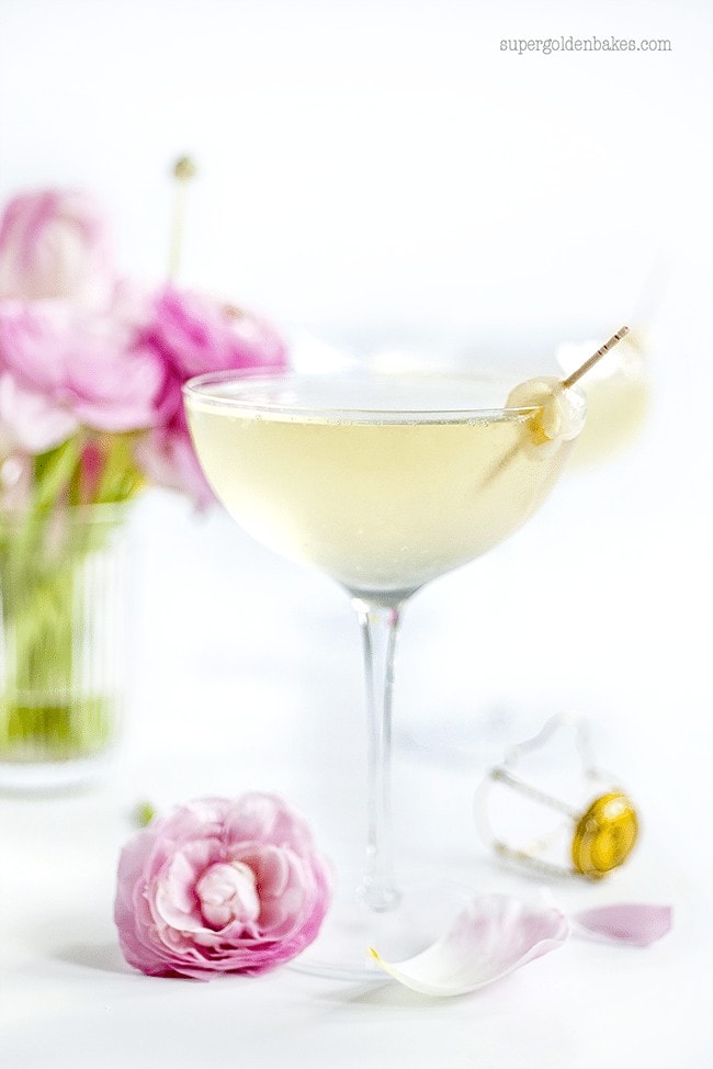 Lychee French 75 Cocktail in a champagne glass with a pink flower beside it.