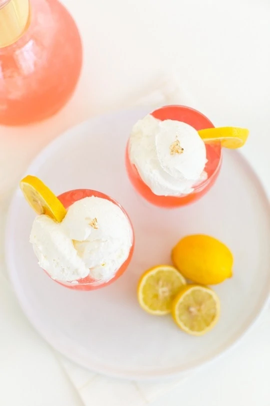 Pink Dream Cocktail with whip cream on top and lemon slices beside it.