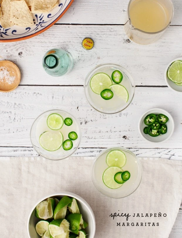 Spicy Jalapeno Margaritas in glasses on a wooden table with limes in a bowl beside them.