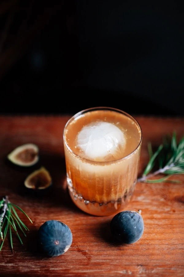 The Fig Old Fashioned with figs beside the glass and a large ice cube inside the drink.