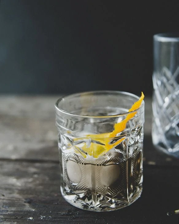 The Violet Hour in a glas with a sprig of orange peel and one large ice cube in it.