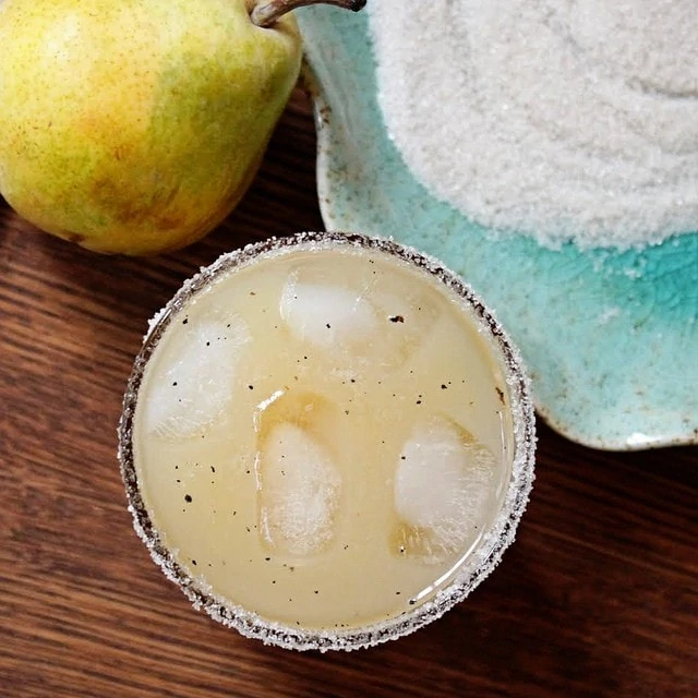 Vanilla, Pear & Vodka Cocktail in a glass with ice cubes and a pear beside the glass.