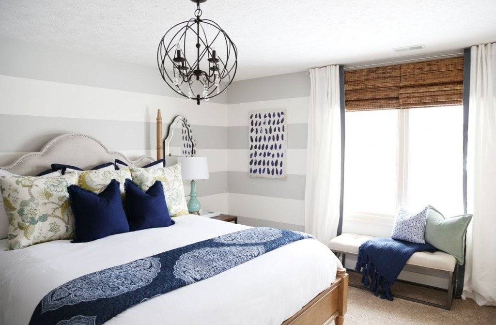 A gues bedroom with blue and white pillows and bedspread, plus a black and crystal globe chandelier over the bed.