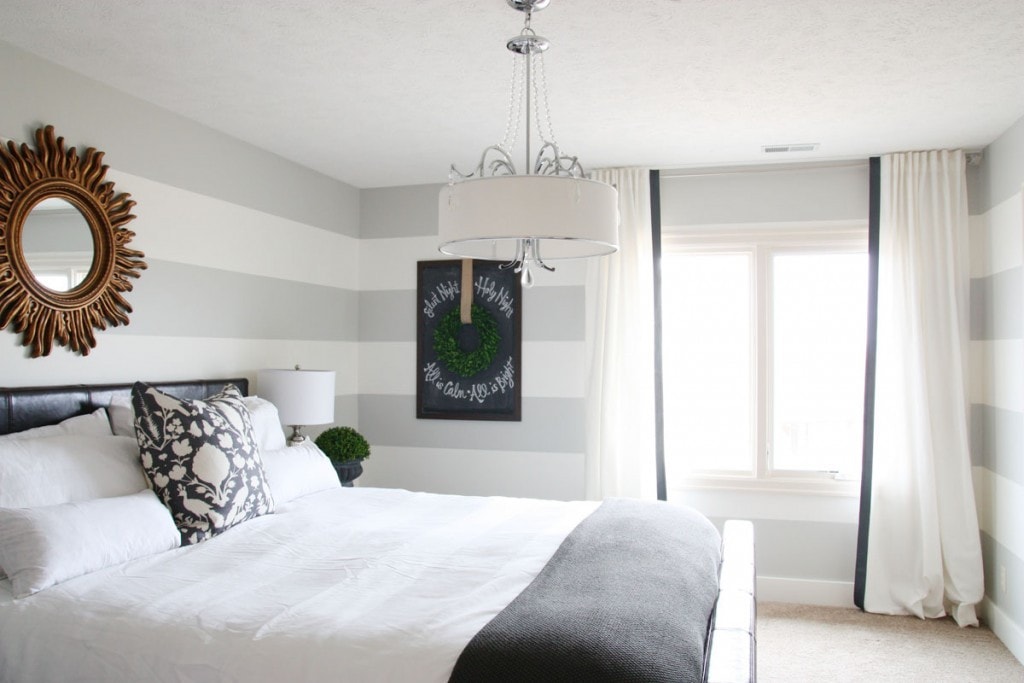 A mostly white bedroom with a gold mirror at the head of the ed, and a chandelier over the bed.