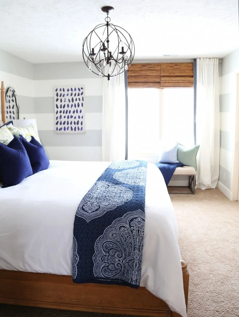 Bamboo shades on the window, blue pillows on the bed, and a round chandelier over the bed.