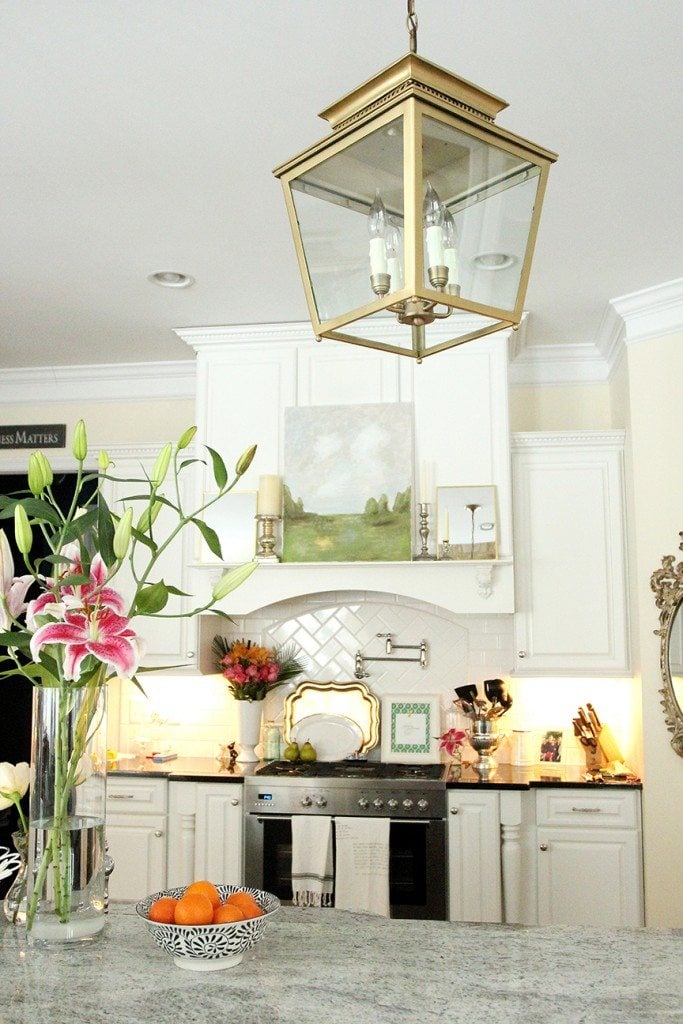 A white traditional kitchen with a large brass light fixture above the island.
