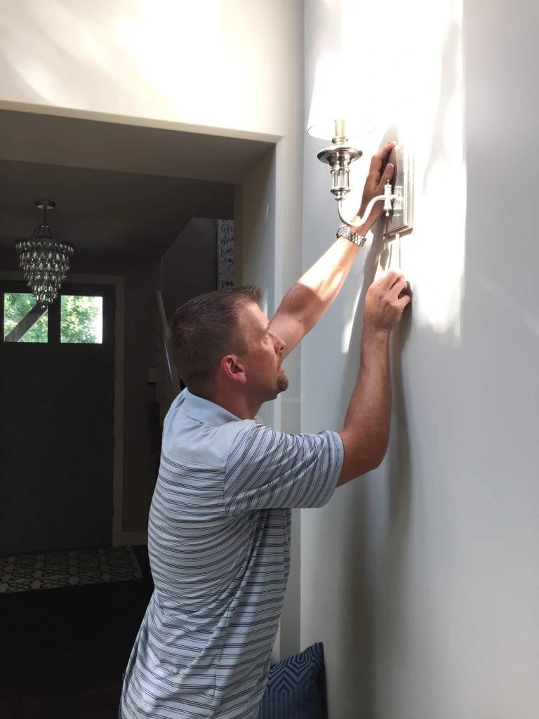A man replacing the sconce in the hallway.