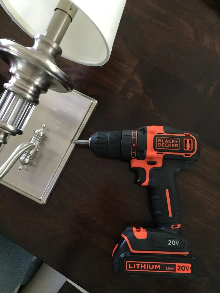 The cordless Black & Decker drill on the floor beside the sconce.