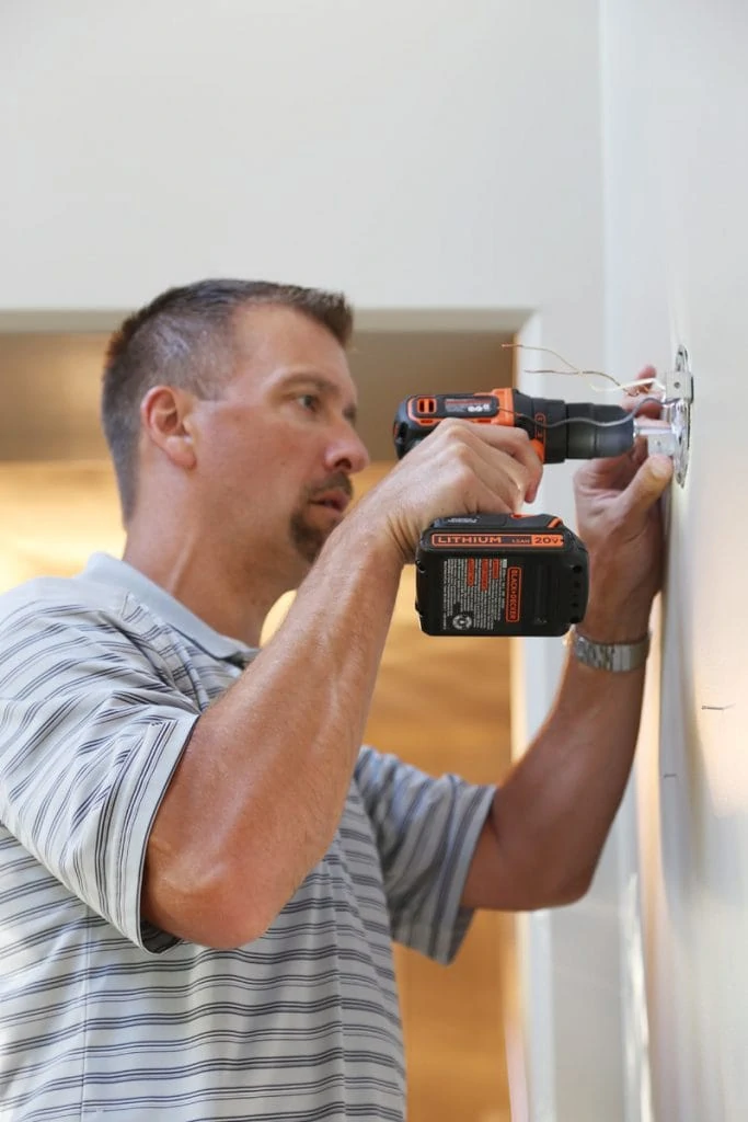 A man using the  Black+Decker Drill to drill where the new sconce will go.