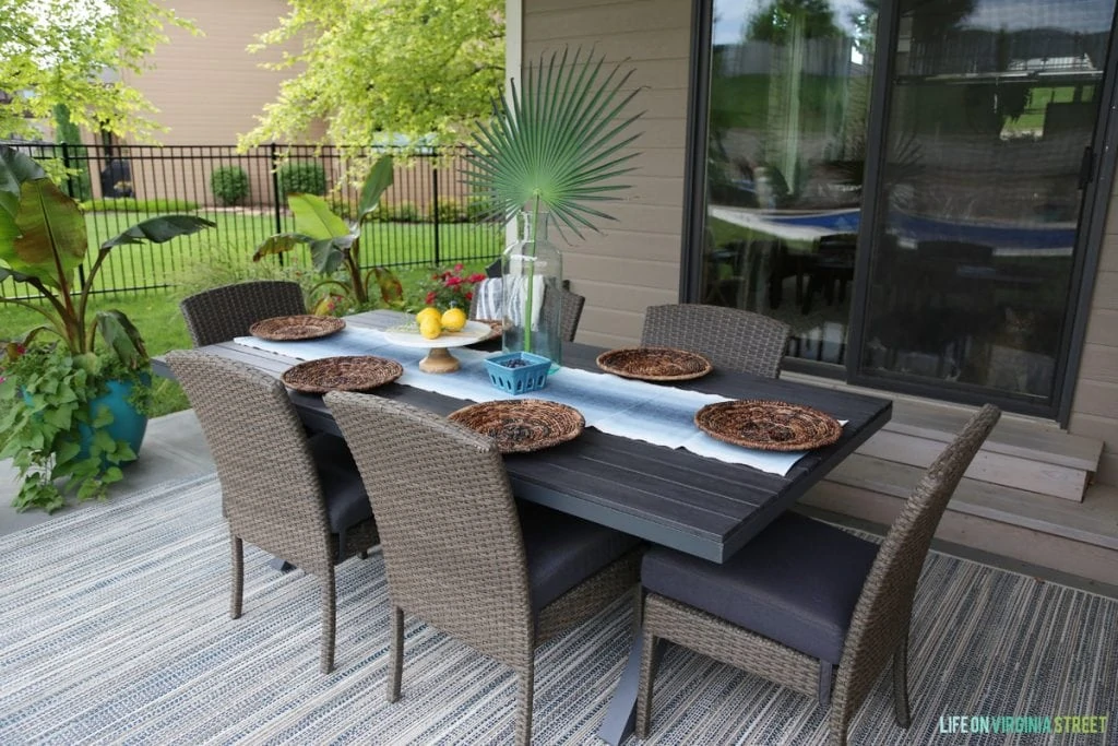 Outdoor table setting before the decor change with lots of brown, table, chairs and rug.