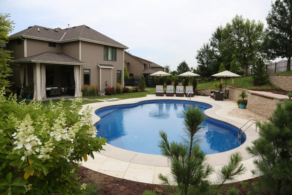 A large backyard pool with shrubs around it.
