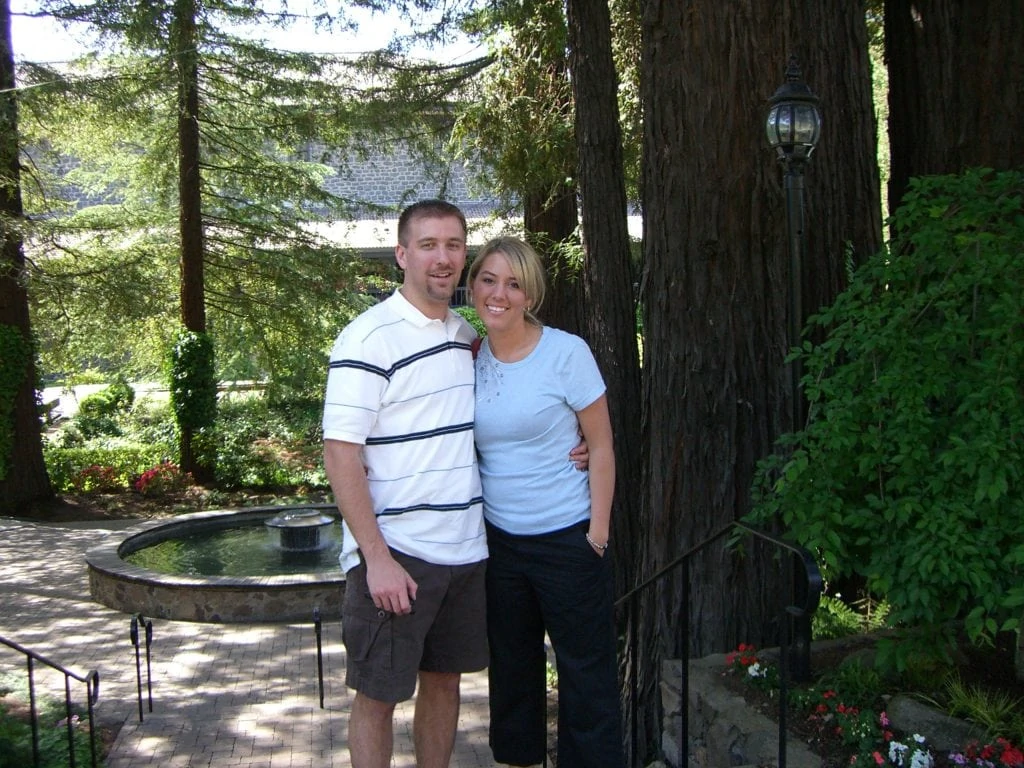 The happy couple posing by large trees.