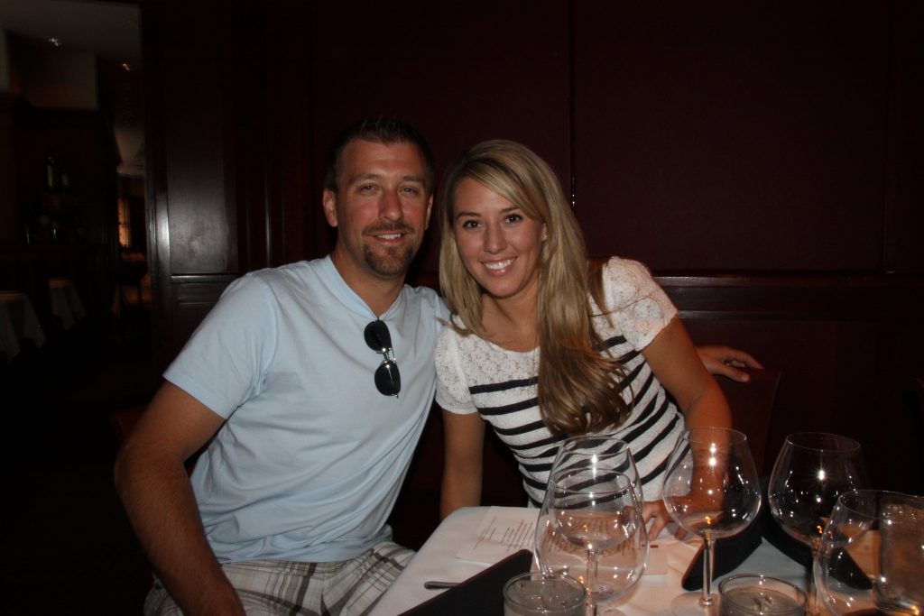 The couple posing with wine glasses in front of them.