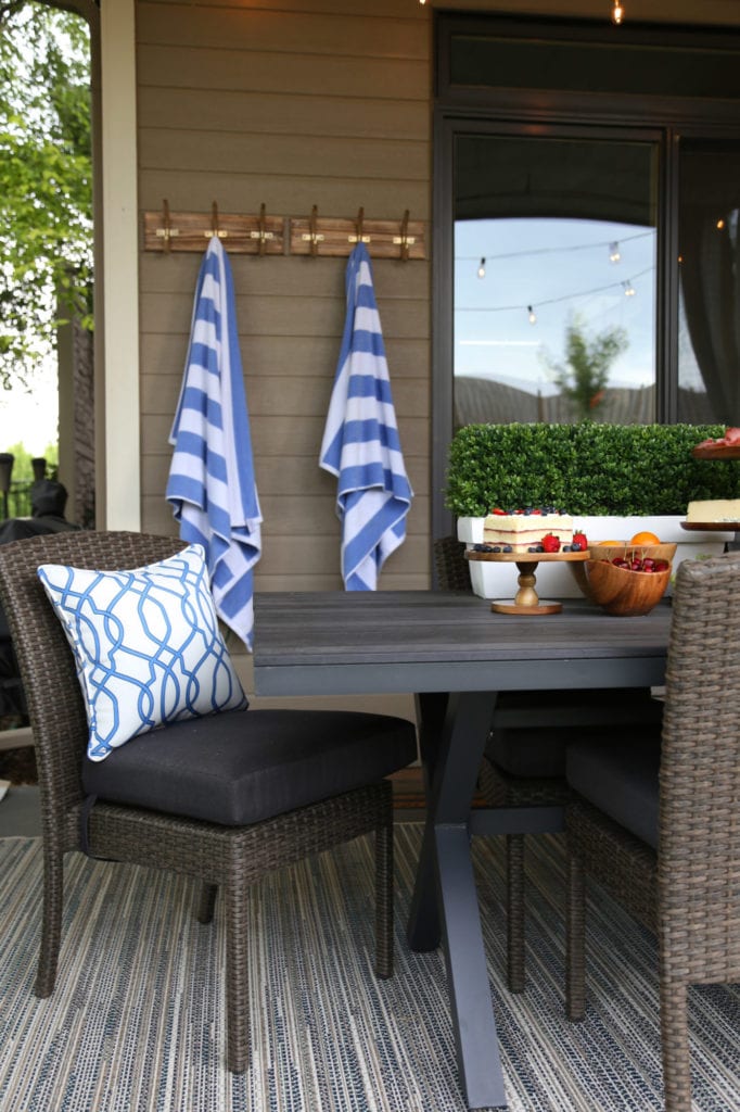 Outdoor dining space with brown wicker and wood dining table, blue and white striped towels, blue and white trellis pillow and blue, brown and gray outdoor rug. 