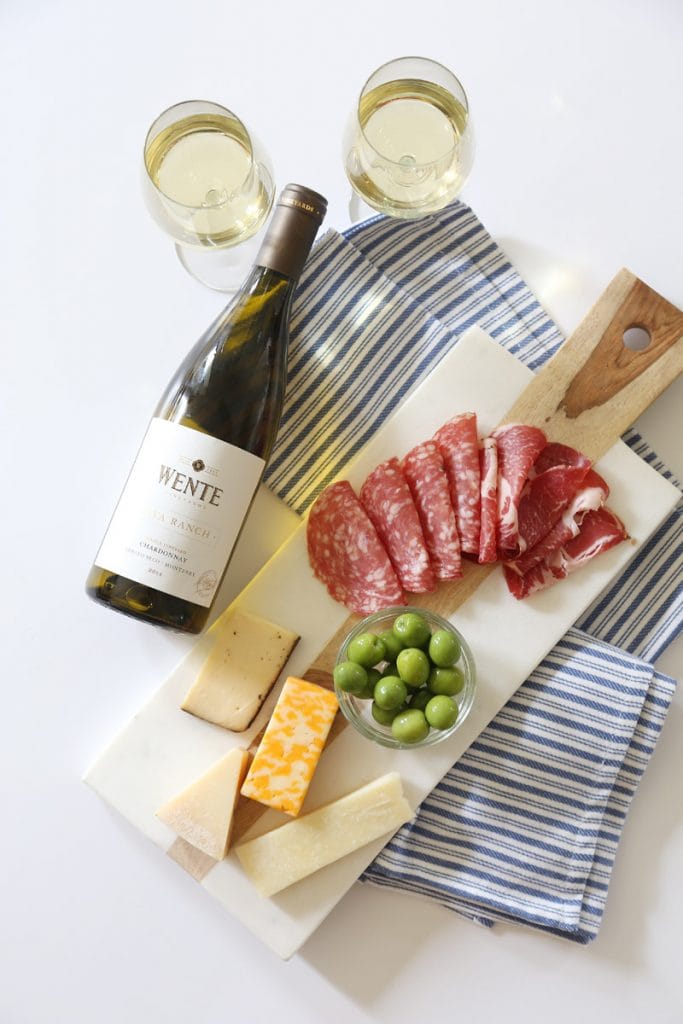A bottle of wine, a cheese and meat platter on the table.