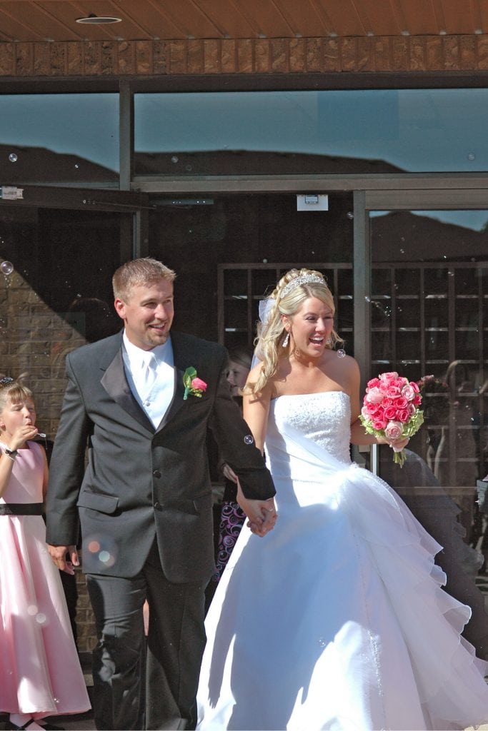 A husband and wife just married holding pink flowers and bubbles all around the happy couple.