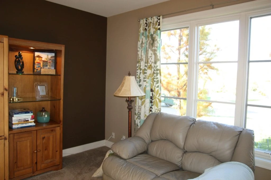 A white leather couch in front of the window in the office with a wooden shelving unit on the adjacent wall.