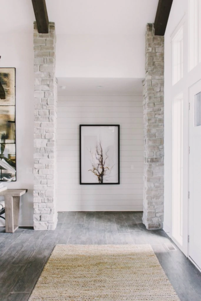 Neutral living entryway with vaulted ceilings, wood beams, white walls and sisal rug. Omaha Street of Dreams. Image via Mandy McGregor Photography.